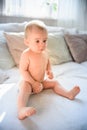 Cute baby girl sits straight on couch in diaper 8th month