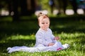 Cute baby girl sitting on the green grass in the city park at warm summer day. Royalty Free Stock Photo