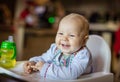 Cute baby girl sitting in high chair and eating piece of bread