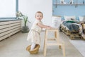 The cute baby girl stand on a straw hat and leans on a wooden chair