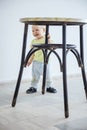 Cute baby girl standing while gripping leg of stool and laughing