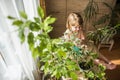 A cute baby girl takes care of houseplants. Girl watering and spraying indoor plants at home Royalty Free Stock Photo