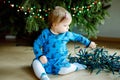 Cute baby girl taking down holiday decorations from Christmas tree. child holding light garland. Family after Royalty Free Stock Photo