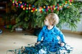 Cute baby girl taking down holiday decorations from Christmas tree. child holding light garland. Family after Royalty Free Stock Photo