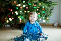 Cute baby girl taking down holiday decorations from Christmas tree. child holding light garland. Family after Royalty Free Stock Photo