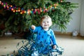 Cute baby girl taking down holiday decorations from Christmas tree. child holding light garland. Family after Royalty Free Stock Photo