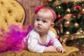 Cute baby girl wearing pink skirt and red headband, laying on couch in front of christmas tree. Royalty Free Stock Photo