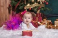 Cute baby girl wearing pink skirt and red headband, lying on white carpet near christmas trees. Christmas gifts. Royalty Free Stock Photo