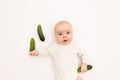 Cute baby girl in white Boda on a white isolated background eating cucumbers, first bait, baby 3-6 months among vegetables, space Royalty Free Stock Photo