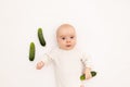 Cute baby girl in white Boda on a white isolated background eating cucumbers, first bait, baby 3-6 months among vegetables, space Royalty Free Stock Photo