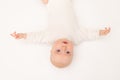 Cute baby girl in a white bodysuit on a white isolated background looking at the camera, baby 3 months old lying on the bed upside Royalty Free Stock Photo