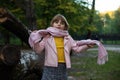 Cute baby girl wraps up in a pink scarf in an autumn Park and plots to play pranks