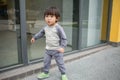 Cute baby in gray suit and green shoes standing and posing in front of glass door Royalty Free Stock Photo