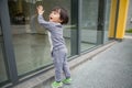 Cute baby in gray suit and green shoes standing and posing in front of glass door Royalty Free Stock Photo