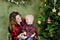 A cute baby and his young mother are laughing and playing, sitting at home near a Christmas tree decorated with Royalty Free Stock Photo