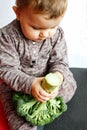 Cute baby holding broccoli in his hands, sitting on the floor indoors