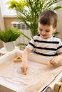 Cute baby little boy drawing smiley fun face on sand table therapy fine motor skills top view Royalty Free Stock Photo