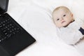 A cute baby is lying on the bed next to a laptop. Parents sit at the computer and look after the child. Copy space - technology Royalty Free Stock Photo