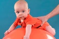 Cute baby lying on the orange fitball on the blue background. Co