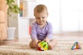 Cute baby playing with colorful toys sitting on carpet in white sunny bedroom. Child with educational toy. Early Royalty Free Stock Photo