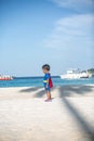 Cute baby in red cape poses as superman on the beach