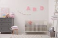 Cute baby room with crib and chest of drawers near white wall Royalty Free Stock Photo