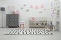 Cute baby room interior with crib and chest of drawers near white wall Royalty Free Stock Photo
