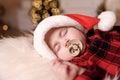 Cute baby in Santa hat with pacifier sleeping on soft faux fur indoors. Christmas season Royalty Free Stock Photo