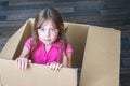 Cute baby is sitting in a cardboard box. The little girl crawled into the mailbox. A baby peeks out of a cardboard parcel