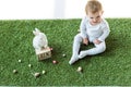 Baby sitting on green grass near wooden calendar with 28 April date, decorative rabbit and colorful Easter eggs isolated Royalty Free Stock Photo