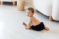 A cute baby is sitting on the white wooden floor in the living room. The little boy toddler is playing at home. The sweet child Royalty Free Stock Photo