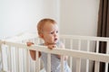 Cute baby standing in a white round bed. White nursery for children. Little girl learning to stand in his crib Royalty Free Stock Photo