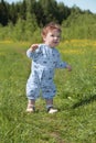 Cute baby stands on green grass near forest