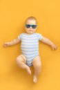 Cute baby with sunglasses lying on an orange dress wearing baby sailor suit with blue and white stripes and enjoying sunbathing Royalty Free Stock Photo