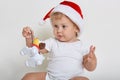 Cute baby wearing christmas hat and body suit playing with plastic dog, charming infant holding his toy, child looking away, baby Royalty Free Stock Photo