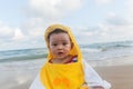 Cute baby wearing a yellow duck cartoon bathrobe sitting and playing on the beach near the sea Royalty Free Stock Photo