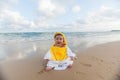 Cute baby wearing a yellow duck cartoon bathrobe sitting and playing on the beach near the sea Royalty Free Stock Photo