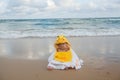 Cute baby wearing a yellow duck cartoon bathrobe sitting and playing on the beach near the sea Royalty Free Stock Photo