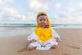 Cute baby wearing a yellow duck cartoon bathrobe sitting and playing on the beach near the sea Royalty Free Stock Photo