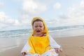 Cute baby wearing a yellow duck cartoon bathrobe sitting and playing on the beach near the sea Royalty Free Stock Photo