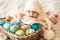 Cute baby in a white knitted cap with a bumbon on a wicker basket. Multi-colored knitting threads. many tangles.