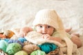 Cute baby in a white knitted cap with a bumbon on a wicker basket. Multi-colored knitting threads. many tangles.