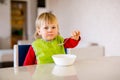 Cute baby 1,4 years old sitting on high children chair and eating vegetable alone in white kitchen