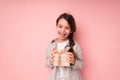 Cute baby 8-9 years old stands on a pink background and rejoices at a small birthday present