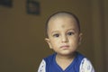 Cute bald indian baby boy in blue and white shirt looking away. Head and shoulder shot. Close up