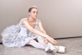 A cute ballerina sitting on the floor with her arms outstretched forward, practicing ballet poses in the studio