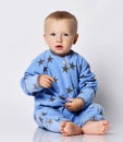 Cute barefooted blond baby boy toddler in blue fleece jumpsuit with stars sits on the floor touching his clothes
