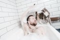 Cute bearded man lies in a bathtub with lush foam when his beloved cat came to him. Royalty Free Stock Photo