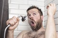 Cute bearded man singing in the bathroom using the shower head with flowing water instead of a microphone Royalty Free Stock Photo