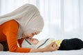 A cute and beautiful Asian Muslim in hijab dress kissing her baby daughter with a tender gesture. Love, care, and relationship Royalty Free Stock Photo